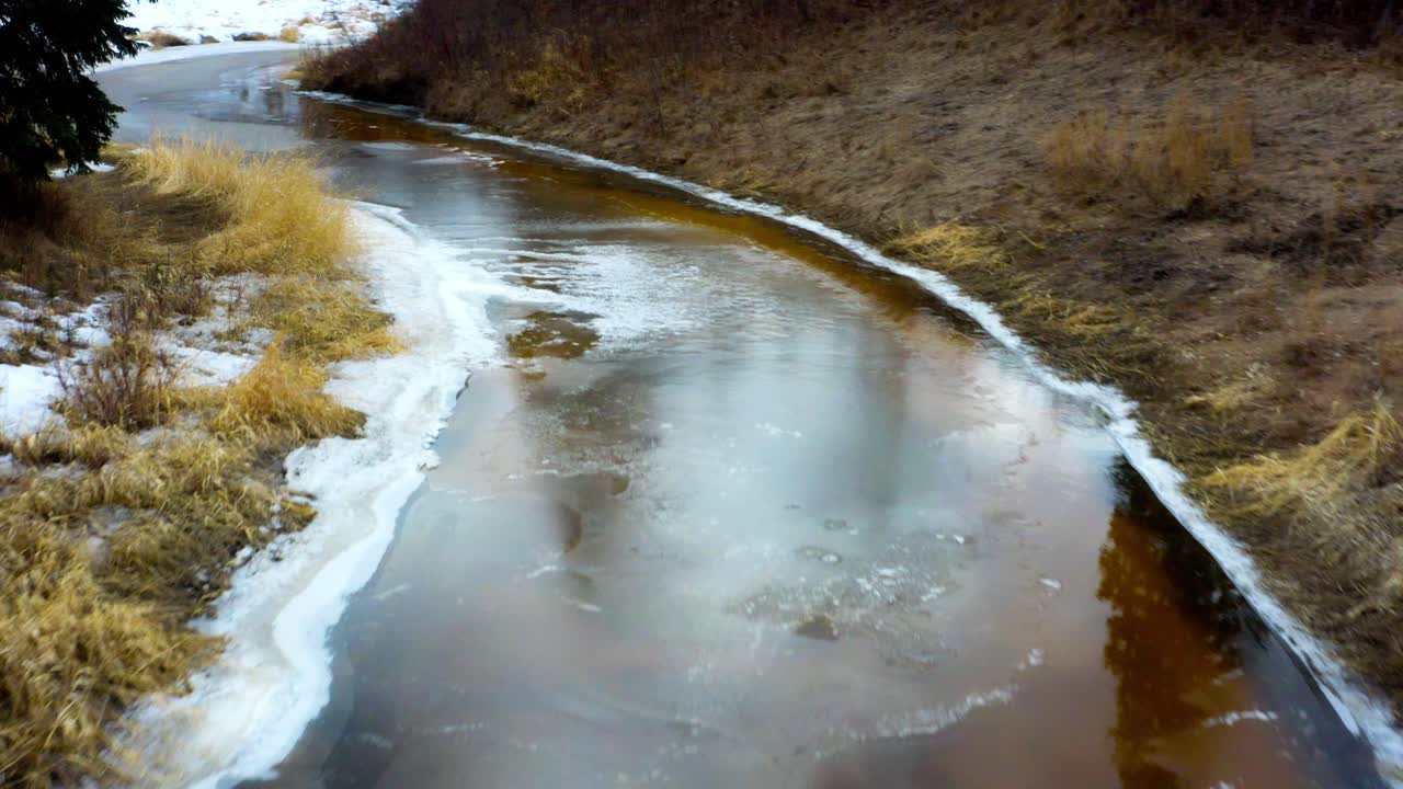 río curvilíneo fusión invernal lodo negro depósitos minerales hielo reflectante ver a través de pino espejado arbustos bosques marrón hierba dorada vía fluvial que conduce al parque de barranco natural cubierto de nieve vida salvaje