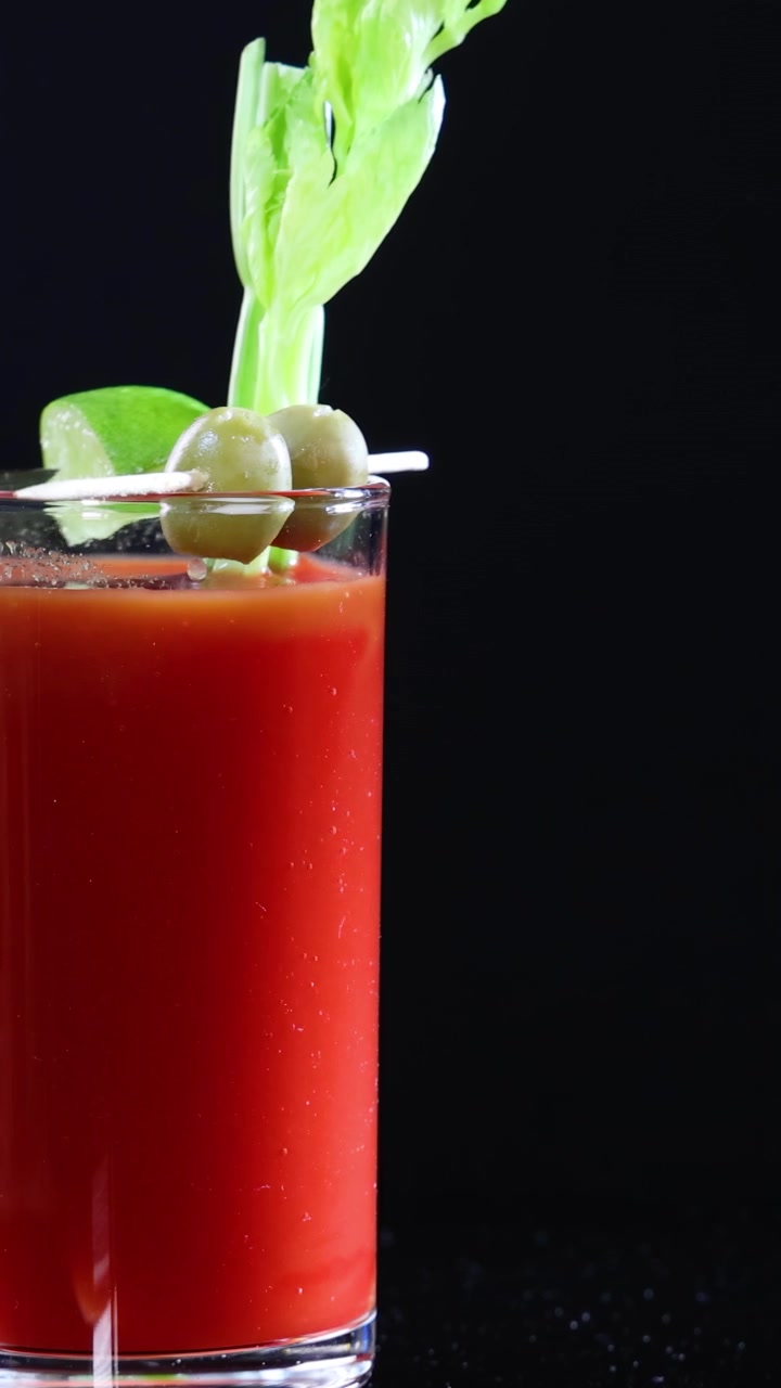 Um coquetel Bloody Mary guarnecido com aipo e azeitonas contra um fundo preto, exibindo cores vibrantes e uma apresentação elegante