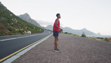 hombre afroamericano actuando estirando las piernas mientras está de pie en la carretera