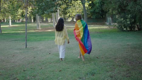 two women walking in a park, covered in a rainbow flag