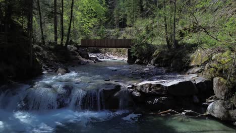 4k aerial drone flight above river with small waterfall towards bridge surrounded by forest