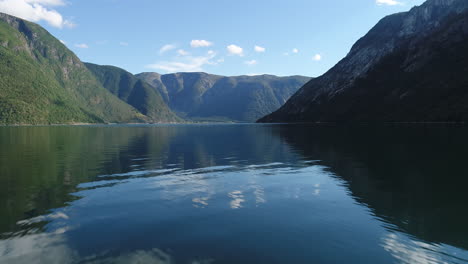 drone flies over calm fjord waters surrounded by towering green mountains under a blue sky. filmed on the west coast of norway during summertime.