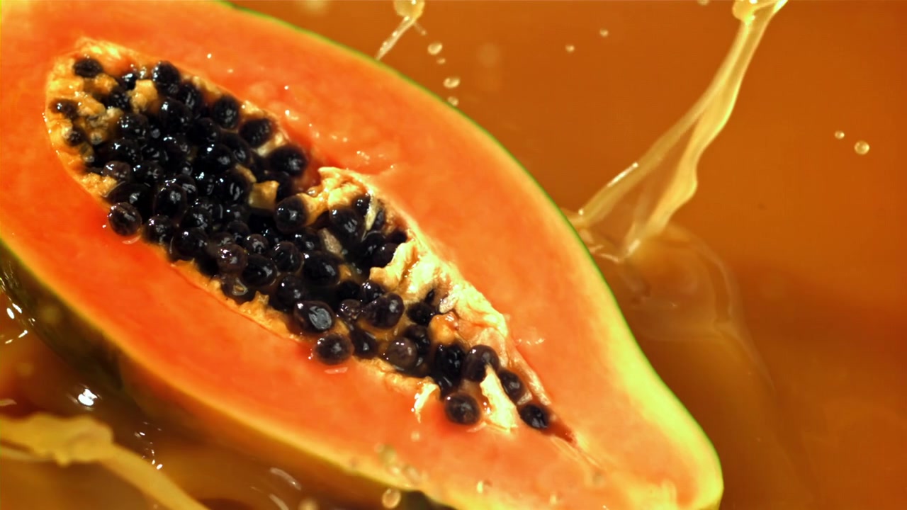 Nærbilde av en halv papaya som plasker ned i appelsinjuice