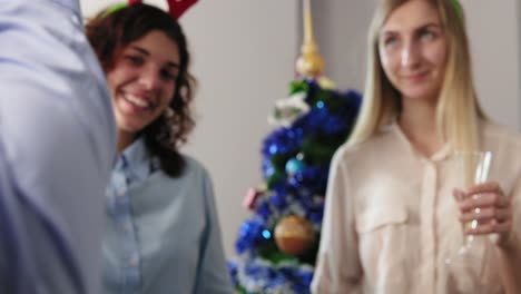 primer plano: manos de un grupo multiétnico de trabajadores de oficina haciendo clic en copas con vino espumoso usando sombreros de navidad durante la nueva