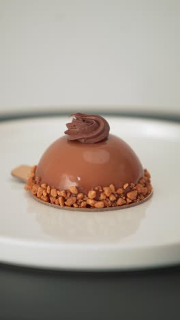 decorating a glossy mousse dessert with a piping bag. elegant pastry topped with chocolate cream, plated on a white dish for refined food visuals