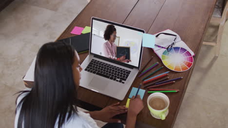 estudiante caucásica usando una computadora portátil en una videollamada con una maestra, tomando notas