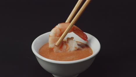 close up of shrimp dipping to shabu shabu dip sauce by chopsticks on the black background