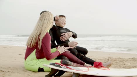 cheerful family in wetsuits sitting in beach