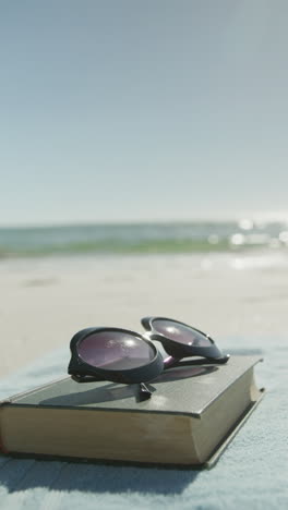 vertical video of book, sunglasses and towel on beach, in slow motion, with copy space