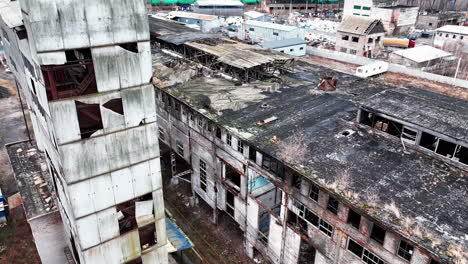 decayed exterior of an old chemical factory complex. grey ruined walls and roofs of the buildings from aerial perspective.