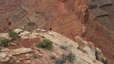 Tiro-De-Drone-De-Mujer-Corriendo-En-La-Cima-De-La-Colina-Sobre-El-Abismo-Y-El-Paisaje-Desértico-De-Utah-Usa