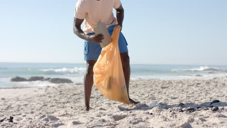 a young african american man cleans up a beach, with copy space