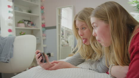 mother with teenage daughter wearing pyjamas lying on bed posing for selfie on mobile phone - shot in slow motion