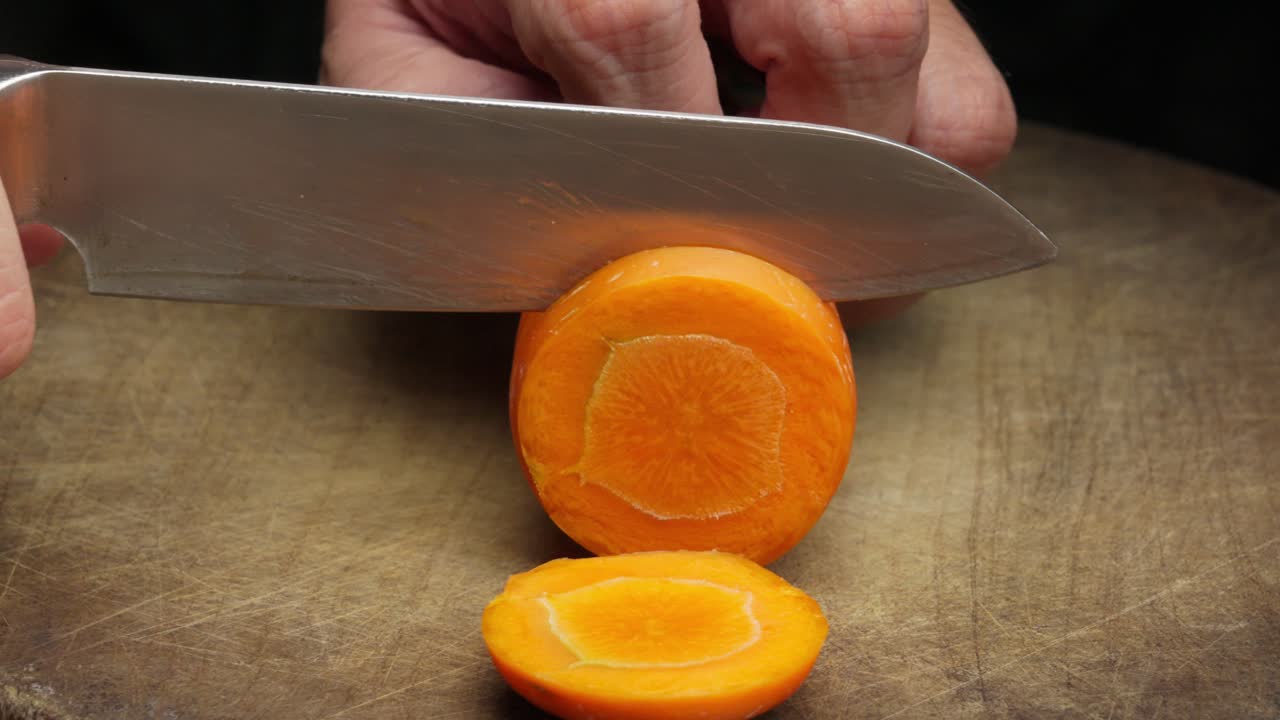 Primo piano, coltello che affetta una carota su un tagliere, preparazione del cibo e mani dello chef