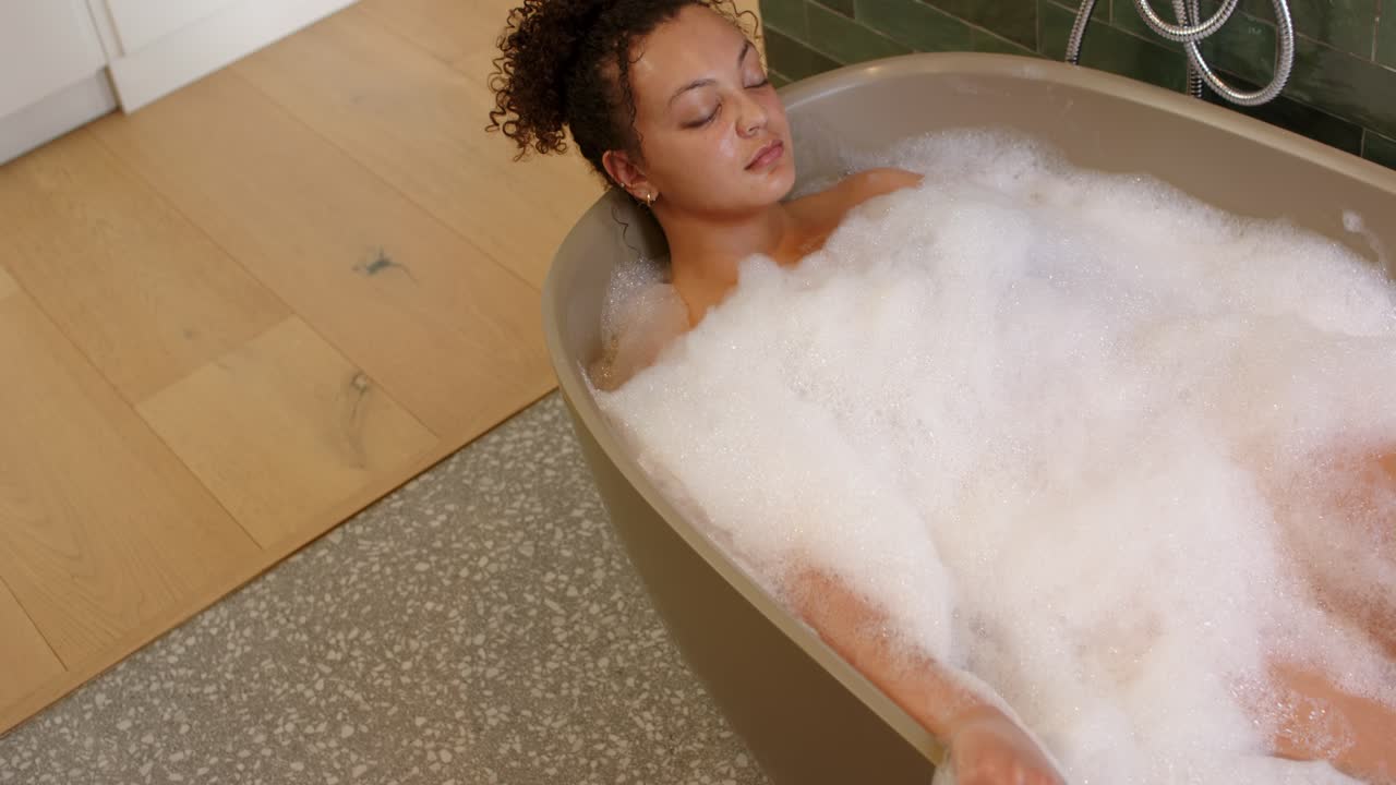 Donna che si immerge in una vasca da bagno autoportante, la telecamera si solleva facendo rilassare la mano, che si adagia nella schiuma, e il rubinetto.