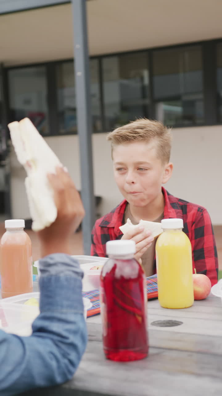 Video verticale di uno scolaro caucasico felice seduto a un tavolo all'aperto che mangia un panino, con spazio per il testo