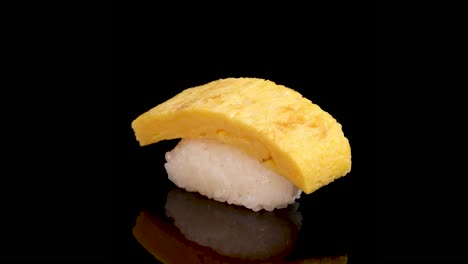 tamago egg sushi rotates smoothly on a glossy black surface, illuminated by soft studio lighting, highlighting texture and detail in a seamless loop