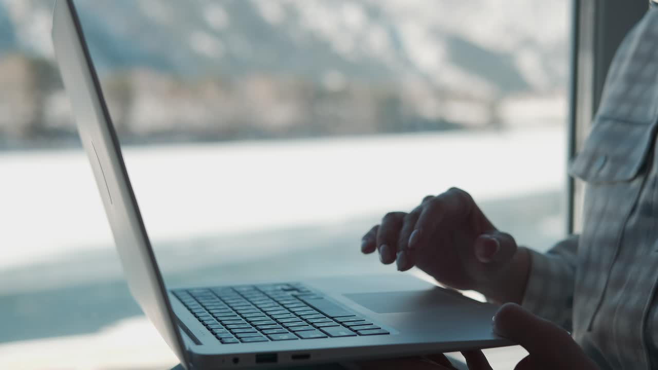 mujer independiente trabajando en casa cerca de la ventana usando una computadora portátil