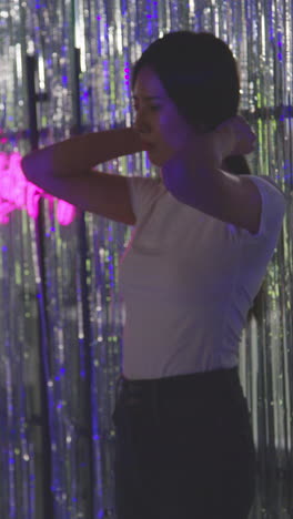 Vertical-Video-Of-Woman-Standing-In-Front-Of-Tinsel-Curtain-In-Nightclub-Or-Funfair