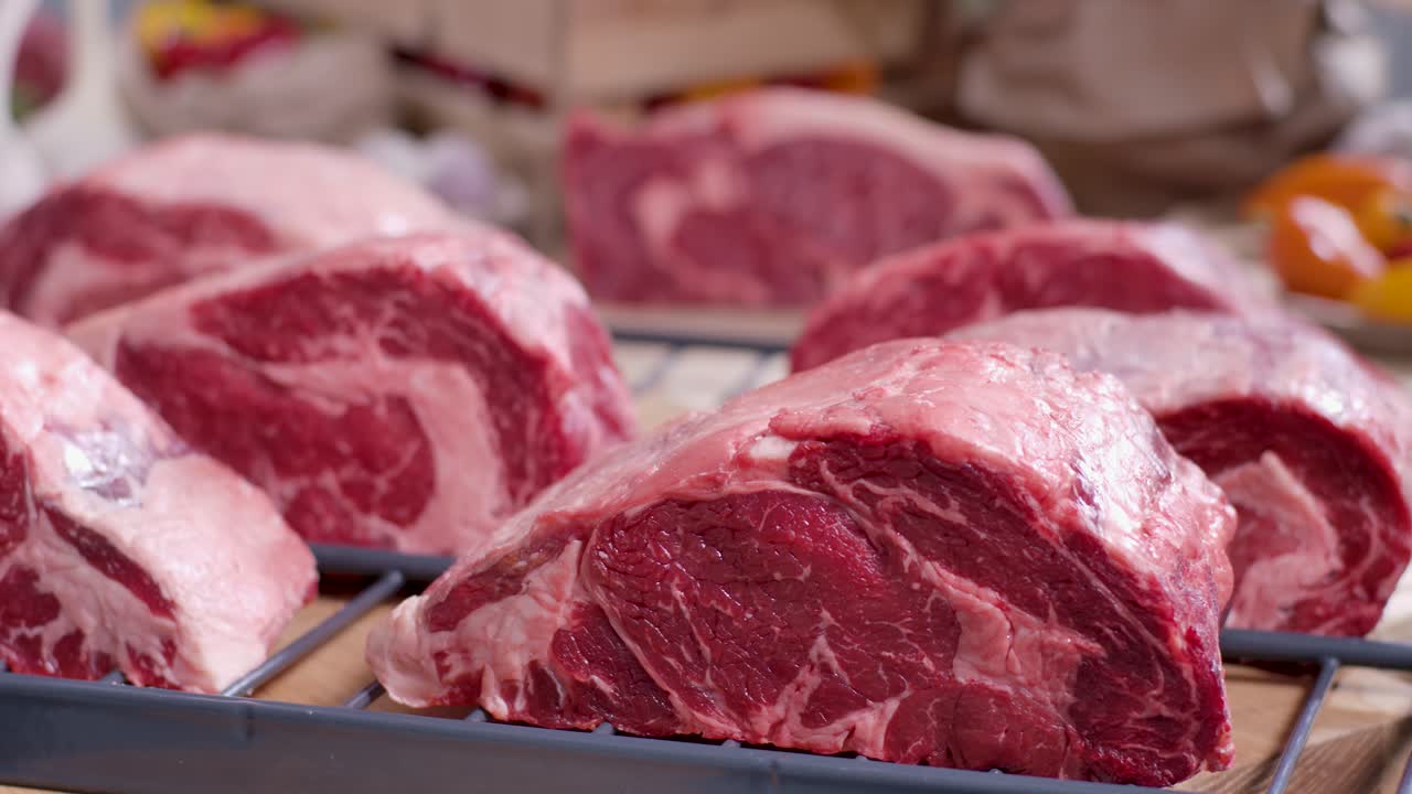 Close up beberapa potong tebal steak ribeye mentah dengan marbling tebal di atas kisi atau rak logam