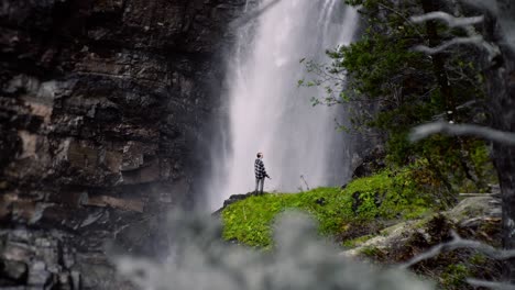 man standing in front of a huge waterfall, enjoying nature on it's finest