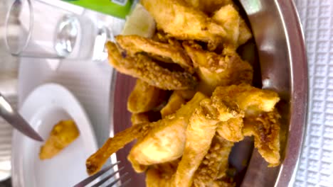 vertical view of a fork pokes a piece of fried food from a silver bowl