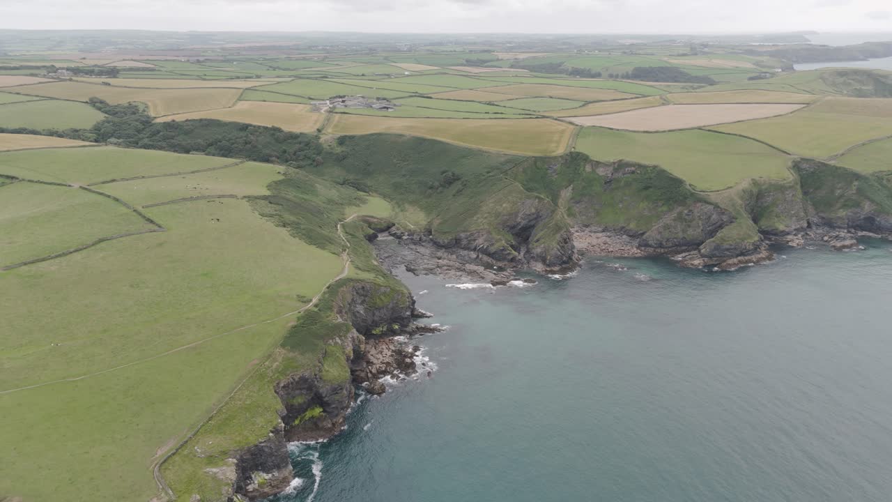 Aerial view of the South West Coast Path winding along the rugged Cornish coastline, with cliffs, fields, and the blue Atlantic Ocean in the background, Cornwall, UK