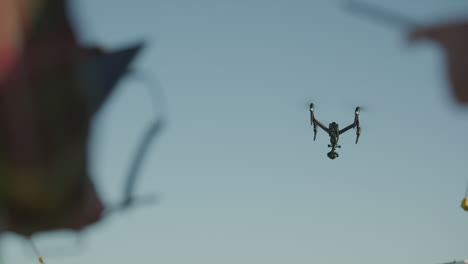 two people standing with a drone in the sky with trees in the background