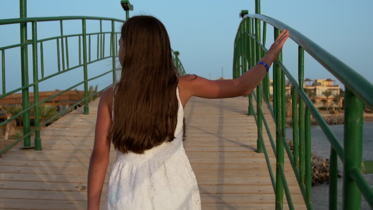 ⁇  드레스를 입은 젊은 여성이 해가 뜨는 시간에 다리를 가로질러  ⁇ 고 있습니다.