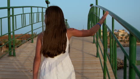 young woman in white dress walking across bridge at sunrise time.