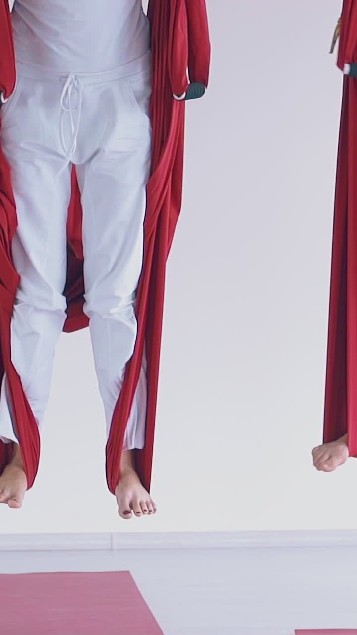 slim women group legs stand on red anti-gravity yoga hammocks cloth in white spacious gym slow motion