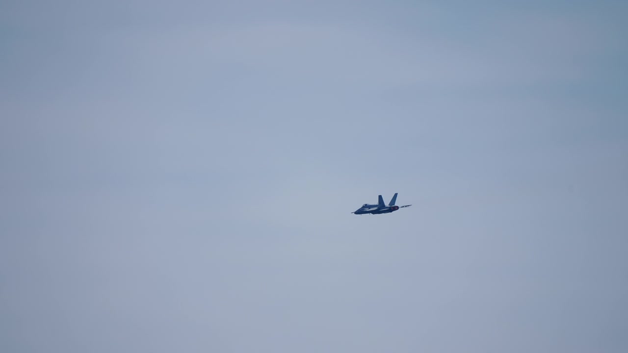 Twin tail fighter jet in distant flight against overcast sky