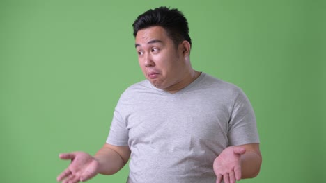 young handsome overweight asian man against green background