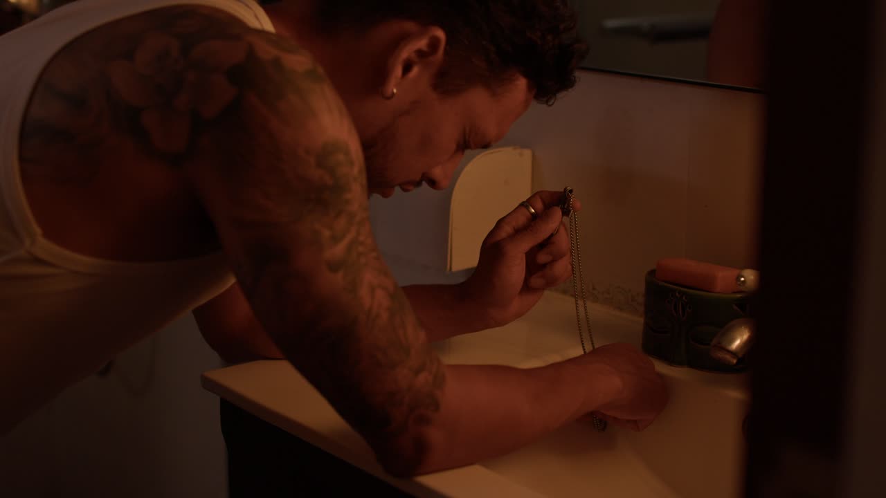 Man with tattoo looking at jewelry in bathroom