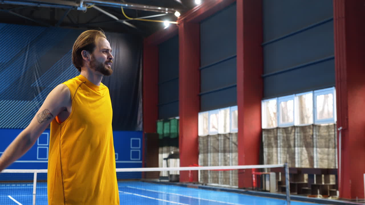 Man in yellow shirt warming up to play pickleball on a blue, inside court