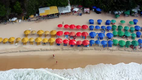 Hermosa-Vista-Aérea-De-Drones-Vista-Superior-Sobrevuelo-De-La-Playa-Tropical-Praia-Do-Madeiro-Con-Coloridas-Sombrillas-De-Playa-Y-Turistas-Nadando-Y-Surfeando-Cerca-De-La-Famosa-Ciudad-De-Pipa-En-El-Norte-De-Brasil