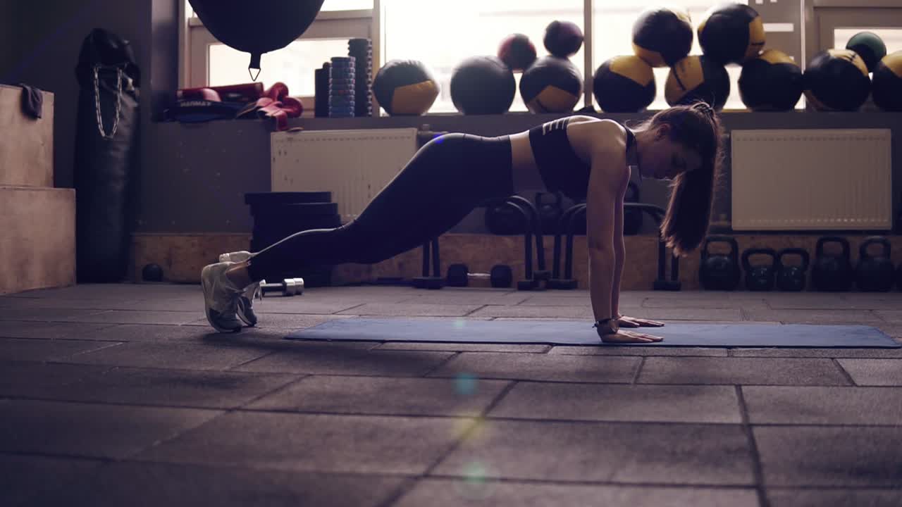 Plank with leg twists workout performed by attractive athletic brunette female in her 20's. Indoors slow motion footage.