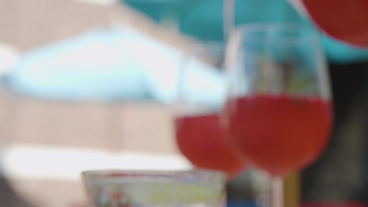 Red cocktail poured into wine glasses outdoors, bright daylight, shallow focus, blue water background
