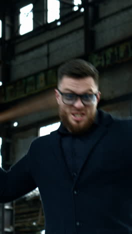 strong bearded young man with bat. guy waves a baseball bat on the background of abandoned house. bandit looks at camera and shouts. vertical video