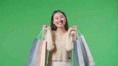 una mujer asiática de compras con bolsas de compras siendo feliz y sonriendo a la cámara mientras está de pie frente a la pantalla verde