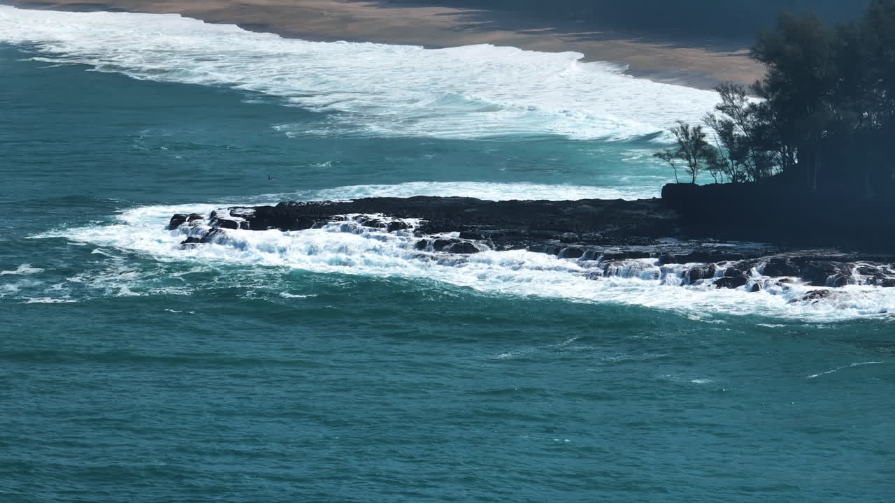 Aerial telezoom of large waves crashing the coastline of Kauai, in sunny Hawaii