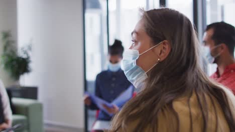 Diverse-group-of-business-colleagues-wearing-face-masks-discussing