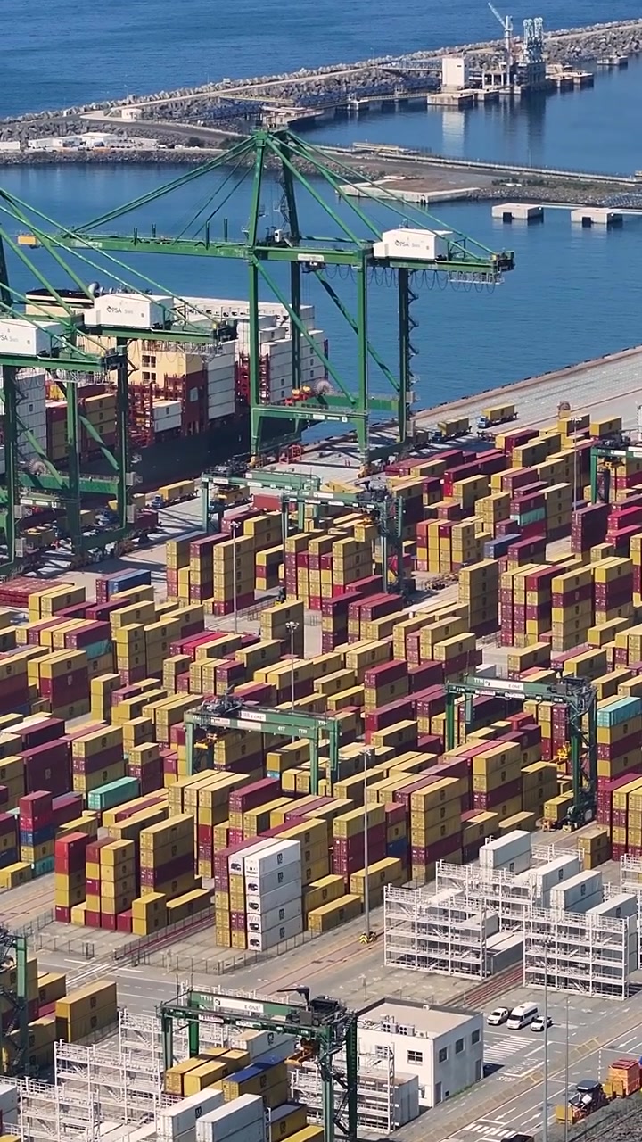 A container terminal with numerous shipping containers stacked and ready for transport. Cranes move cargo at the facility located near the water.