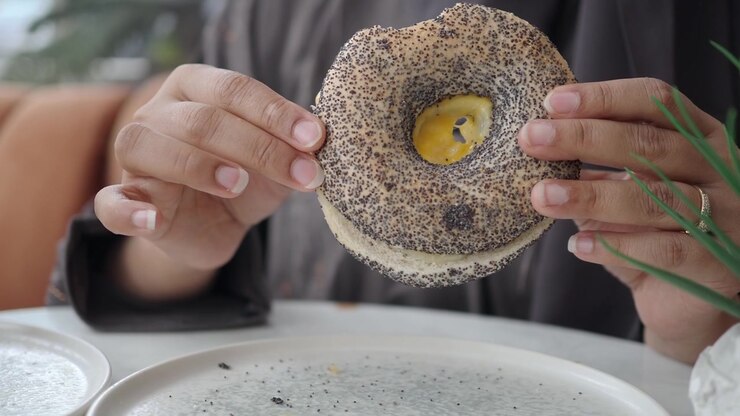 Person Holding a Poppy Seed Bagel with Cream Cheese