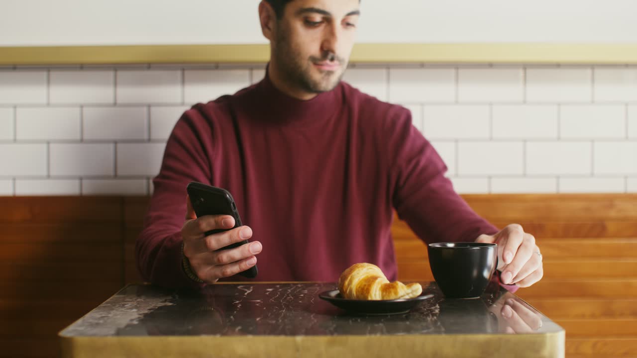 hombre disfrutando del desayuno y usando su teléfono en un café