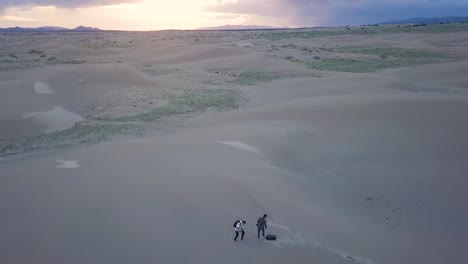 dos fotógrafos escalan una duna de arena en el desierto de mojave, utah al atardecer