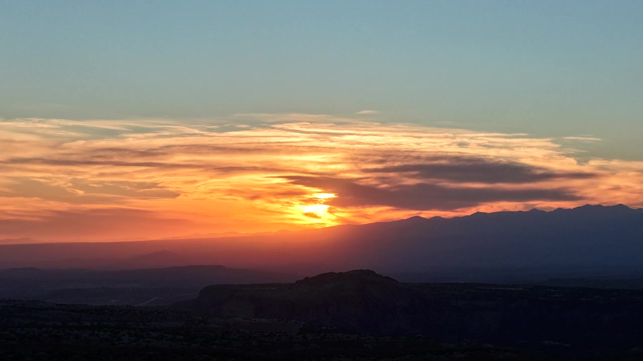 Timelapse 4K UHD con drone che cattura un'alba vibrante. Una luce arancione brillante e dorata illumina nuvole stratificate sopra un canyon desertico scuro e in silhouette e una catena montuosa aspra