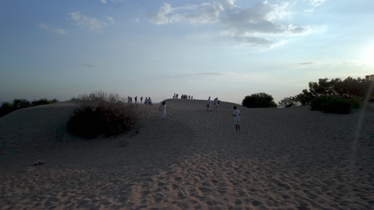 People walking on a sand dune at sunset