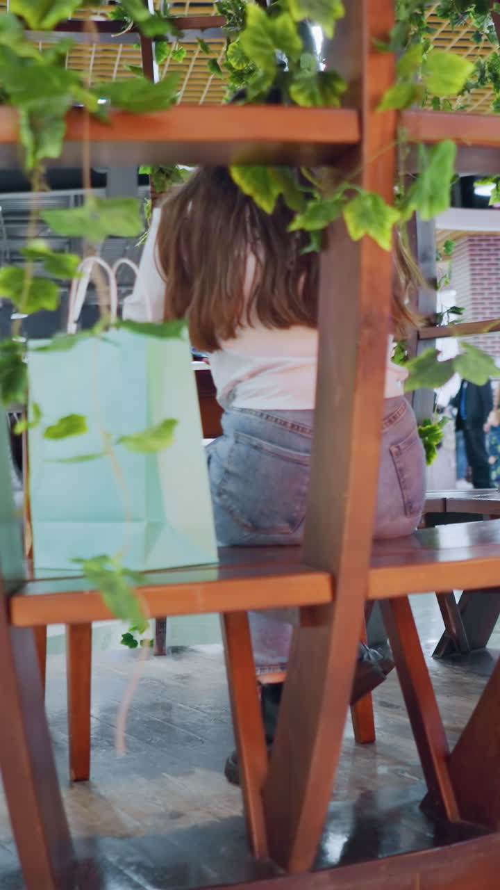 장식 된 나무 좌석에 앉아있는 젊은 여성, 에 쇼핑 가방을 들고, 다른 사람들이 쇼핑몰의 활기차고 바쁜 배경에서 고 앉아 있는 것을 볼 수 있습니다.