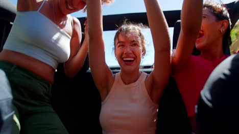 female friends standing up through sun roof of car on road trip through countryside